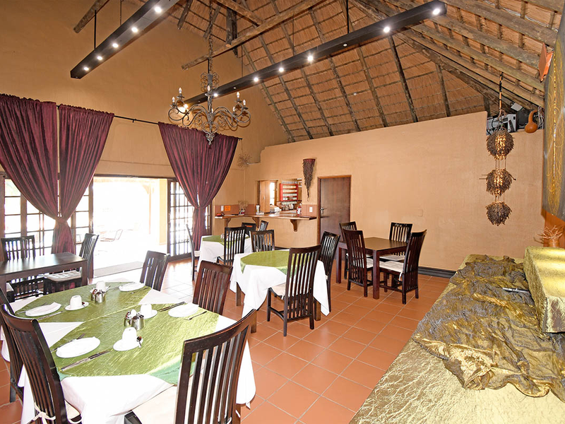 Spacious dining area featuring a high thatched roof with exposed timber rafters, terracotta flooring, and direct access to an outdoor patio through sliding doors.