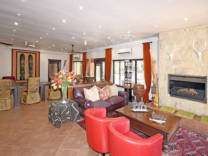 Spacious open-plan living and dining area featuring a prominent stone fireplace, tiled flooring, and integrated downlighting, creating a warm and inviting lodge atmosphere.