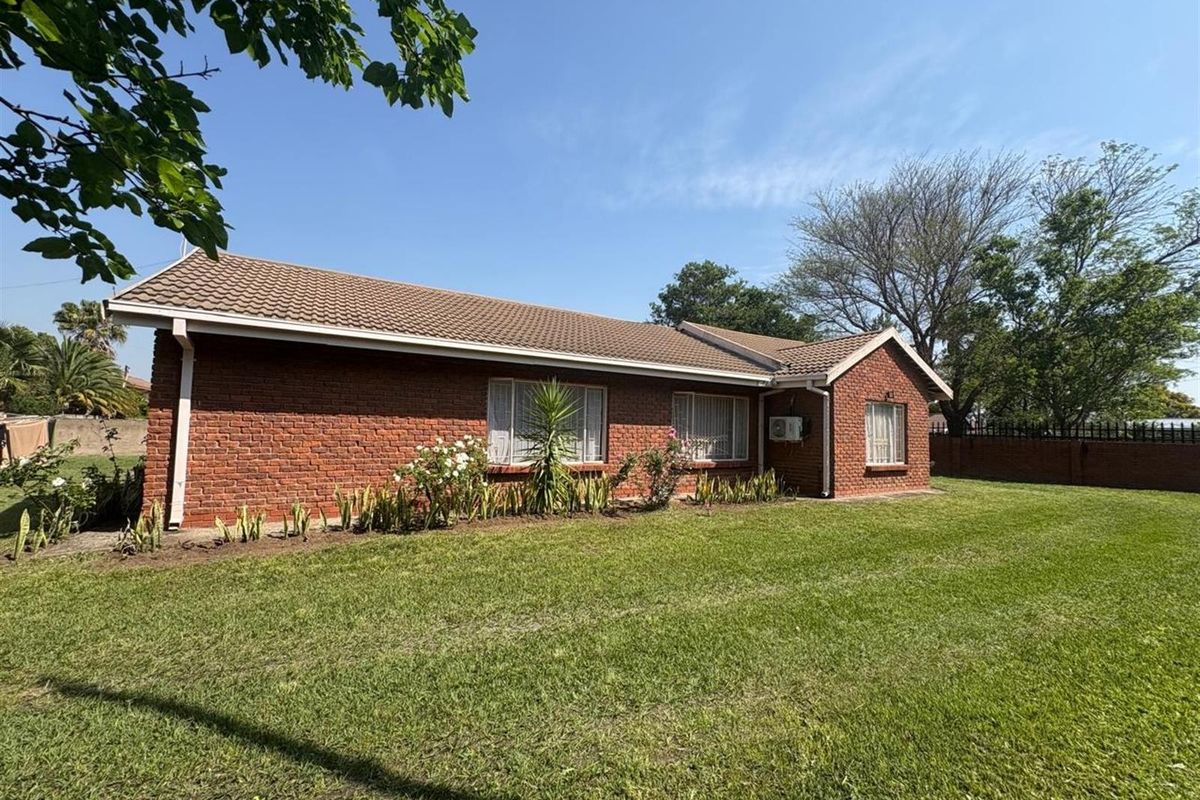 A view of the rear exterior of a single-story brick house featuring a tiled roof, large windows, and a spacious surrounding lawn.