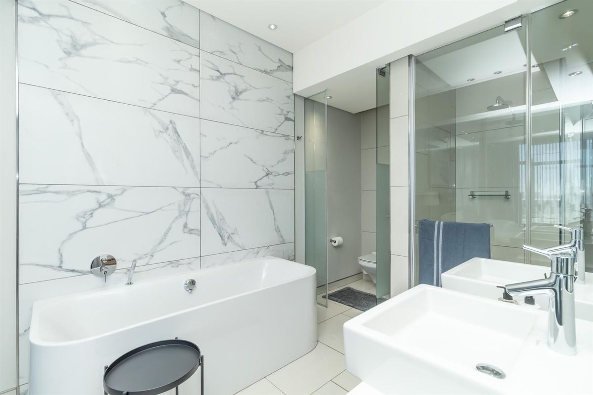 Modern bathroom featuring a freestanding bathtub, dual vanity sinks, and a glass-enclosed shower with marble-effect wall tiling.