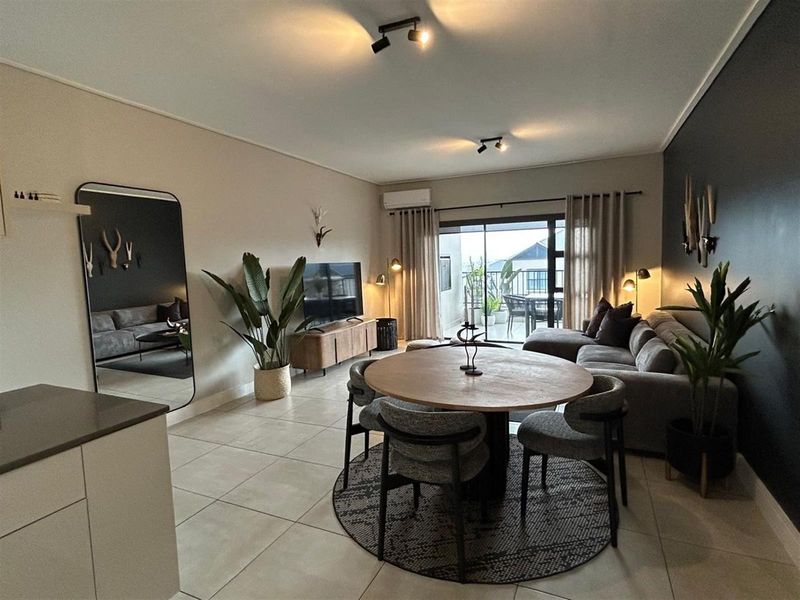 Spacious open-plan living and dining area featuring tiled floors, modern track lighting, and a sliding glass door leading to an outdoor balcony.