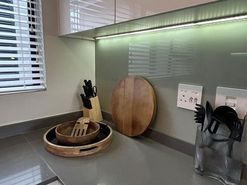 Modern kitchen featuring high-gloss cabinetry, sleek quartz countertops, a glass splashback, and integrated under-cabinet lighting for a clean, contemporary finish.