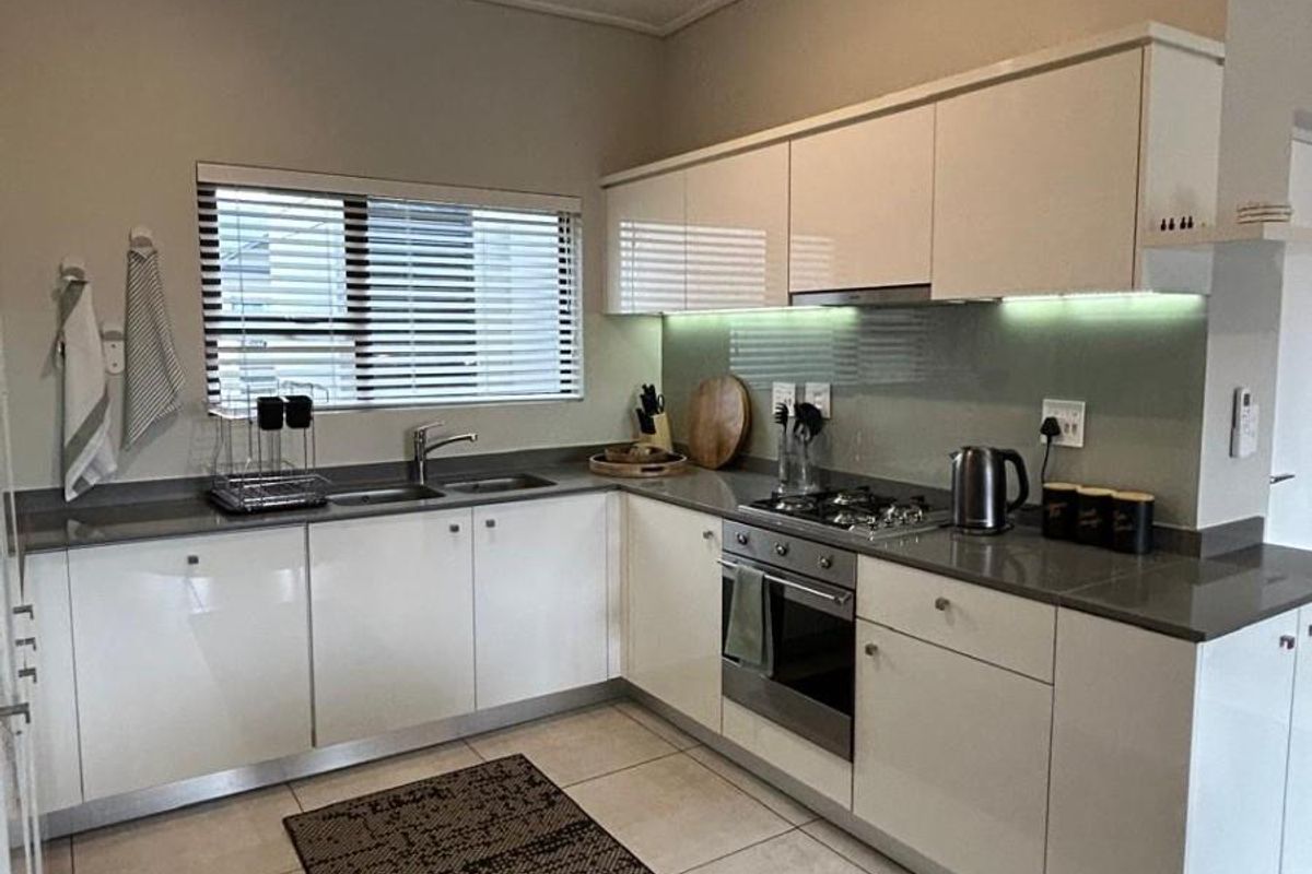 Modern kitchen featuring white high-gloss cabinetry, stone countertops, integrated gas hob, built-in oven, and under-cabinet lighting with neutral tiled flooring.