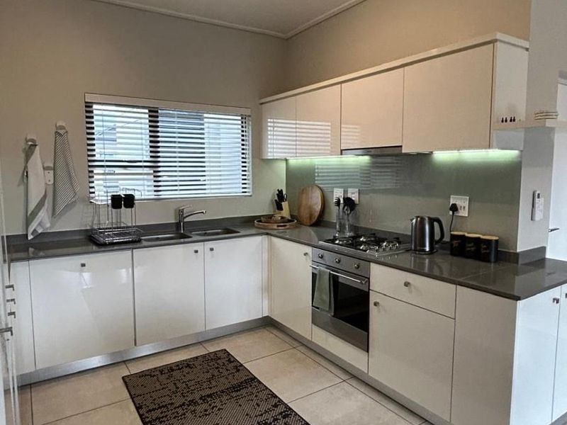 Modern kitchen featuring white high-gloss cabinetry, stone countertops, integrated gas hob, built-in oven, and under-cabinet lighting with neutral tiled flooring.