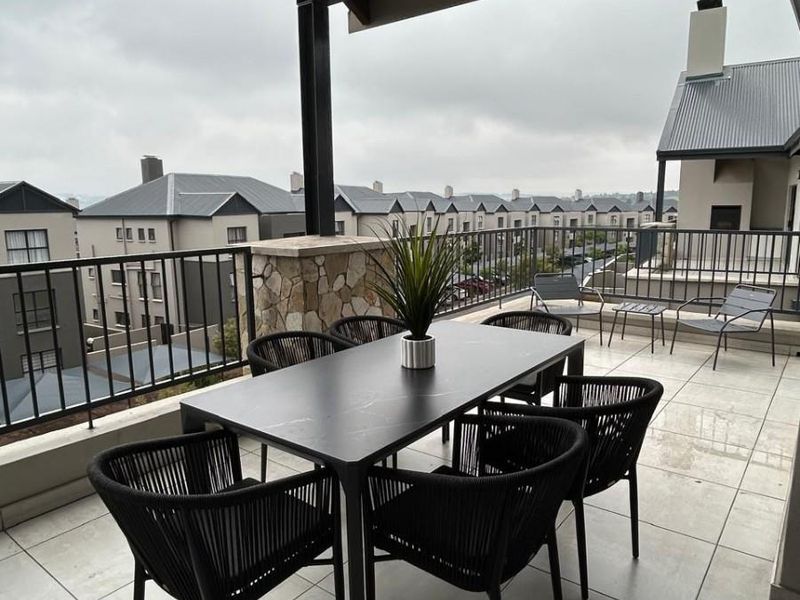 Spacious covered balcony featuring tiled flooring, a stone-clad pillar, and a metal balustrade, offering an elevated outdoor living space with neighbourhood views.