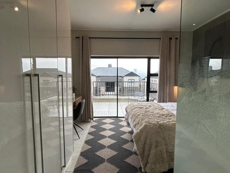 Modern bedroom featuring extensive built-in cupboards, tiled flooring, and large sliding glass doors providing direct access to a private balcony.