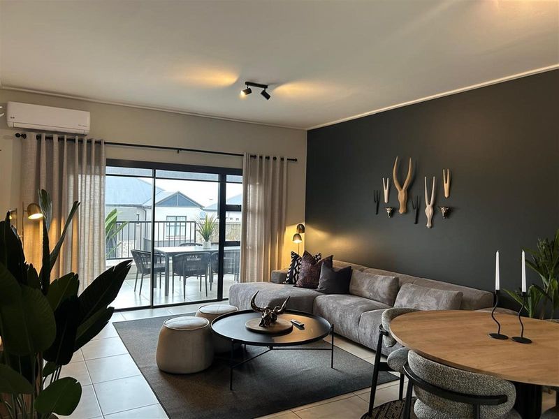 A well-maintained open-plan living area featuring tiled floors, track lighting, and a split-system air conditioner, with direct access to an outdoor balcony.
