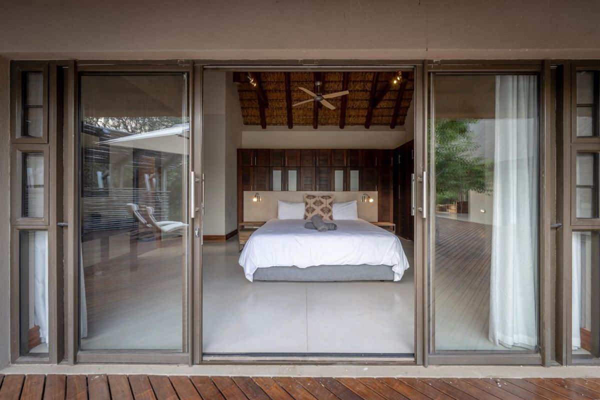 Spacious bedroom featuring polished concrete floors, exposed thatched ceiling with fan, and extensive built-in cabinetry, opening onto a wooden deck through sliding glass doors.