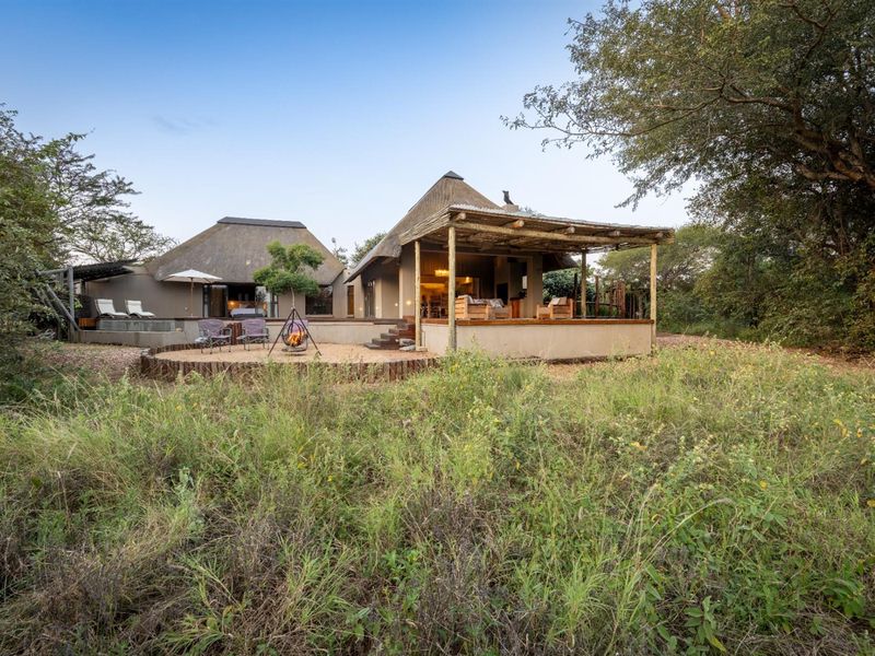 Rear view of a bushveld-style home featuring a thatched roof, expansive covered patio, raised timber deck, and a private plunge pool set in natural surroundings.