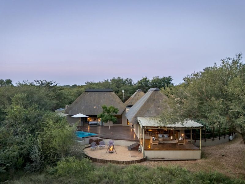 Aerial view of a luxury bushveld lodge featuring thatched roofs, a swimming pool, expansive timber decking, and a dedicated outdoor boma entertainment area.