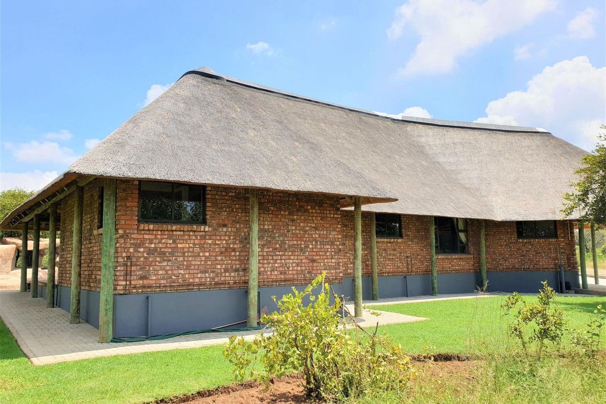 A well-maintained commercial building featuring traditional thatched roofing, exposed face-brick exterior walls, and a covered veranda supported by timber posts.