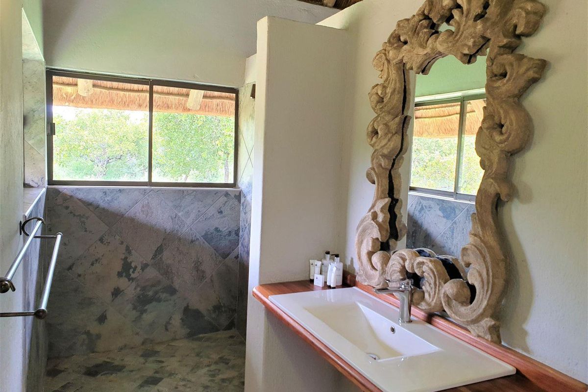 A bathroom featuring a built-in vanity with a basin, slate-style wall and floor tiling, and a thatched roof ceiling.