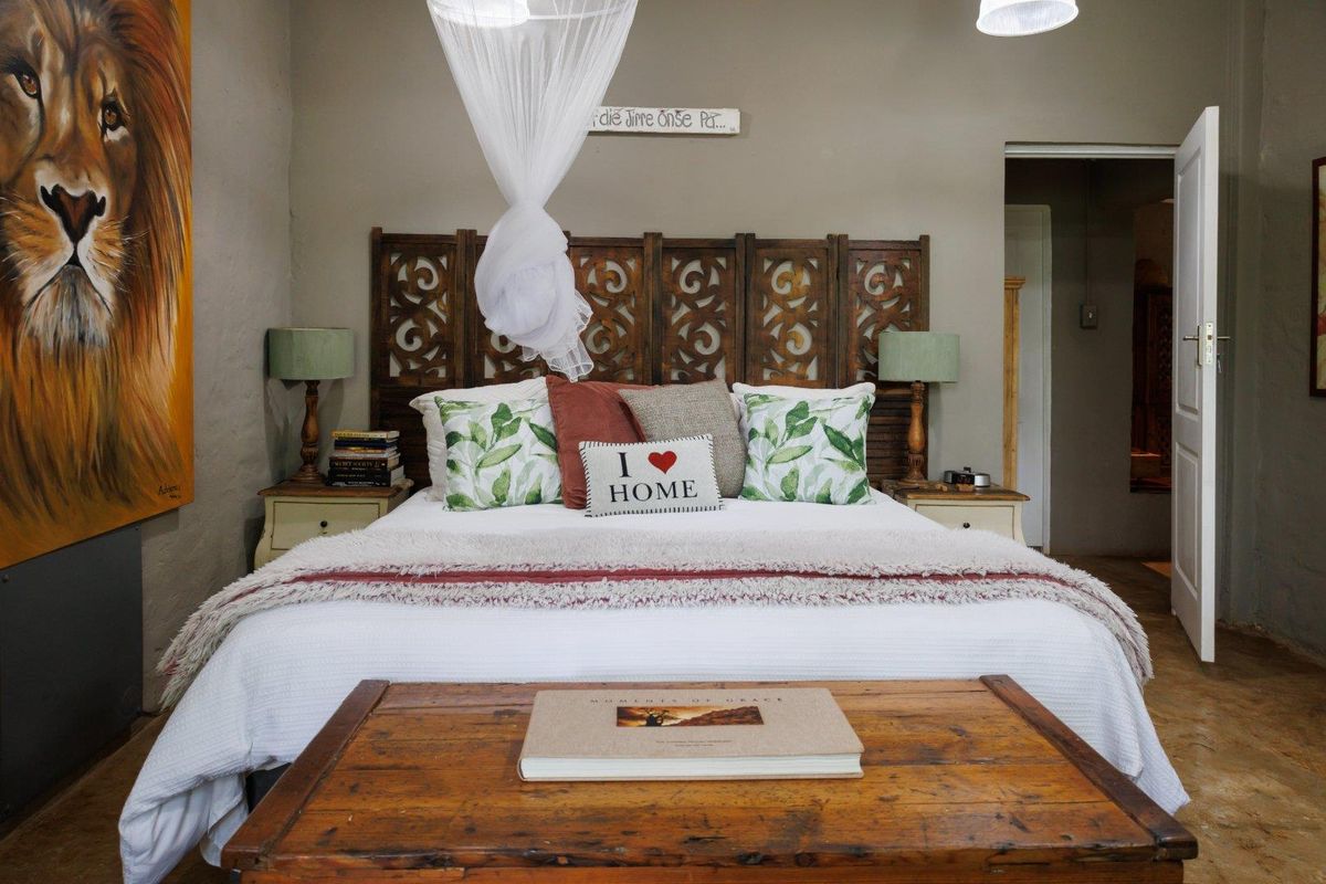 A well-maintained bedroom featuring a decorative carved wooden headboard, neutral wall tones, and direct access to an adjoining room.
