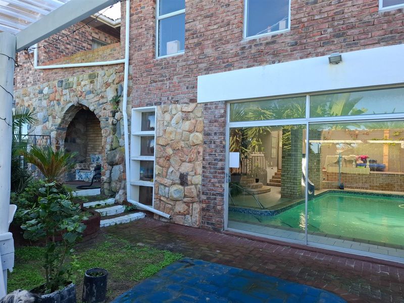 Rear exterior view featuring a swimming pool, exposed brick and stone facade, and a unique arched stone alcove area.