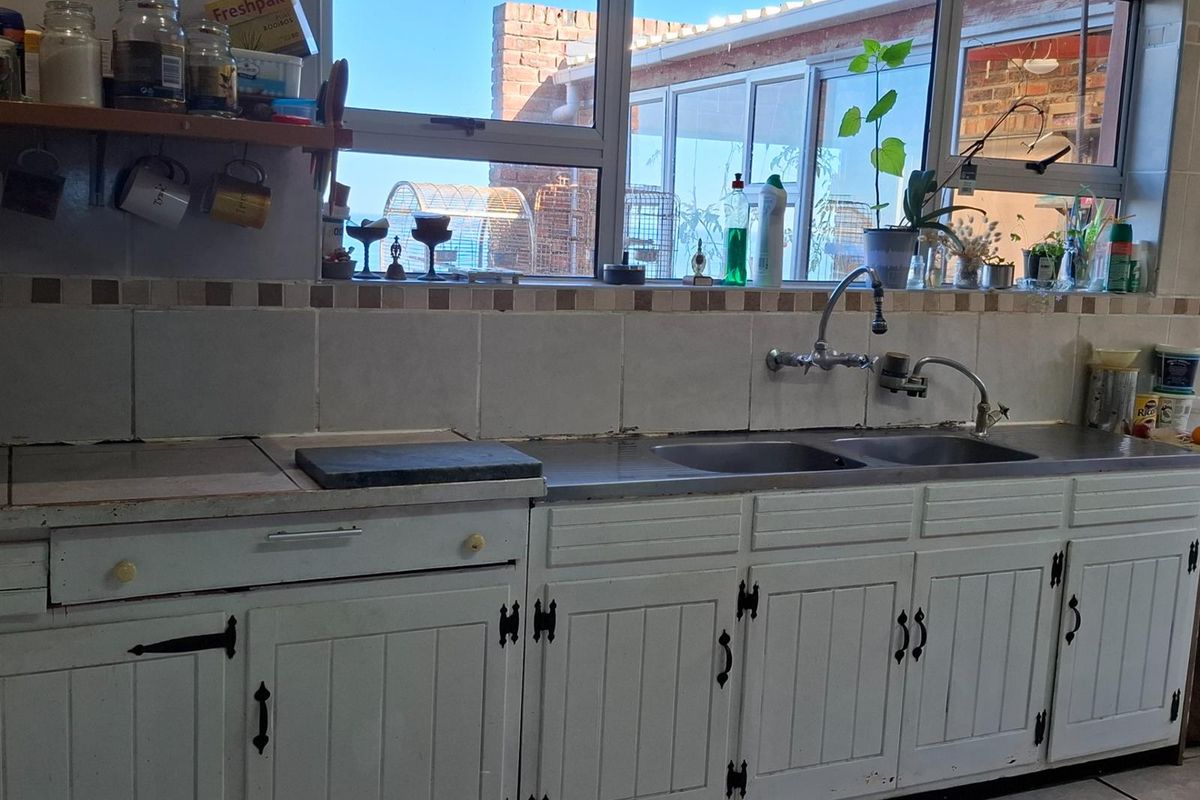 A functional kitchen area featuring a double stainless steel sink, tiled backsplash, and traditional white cabinetry with ample natural light.