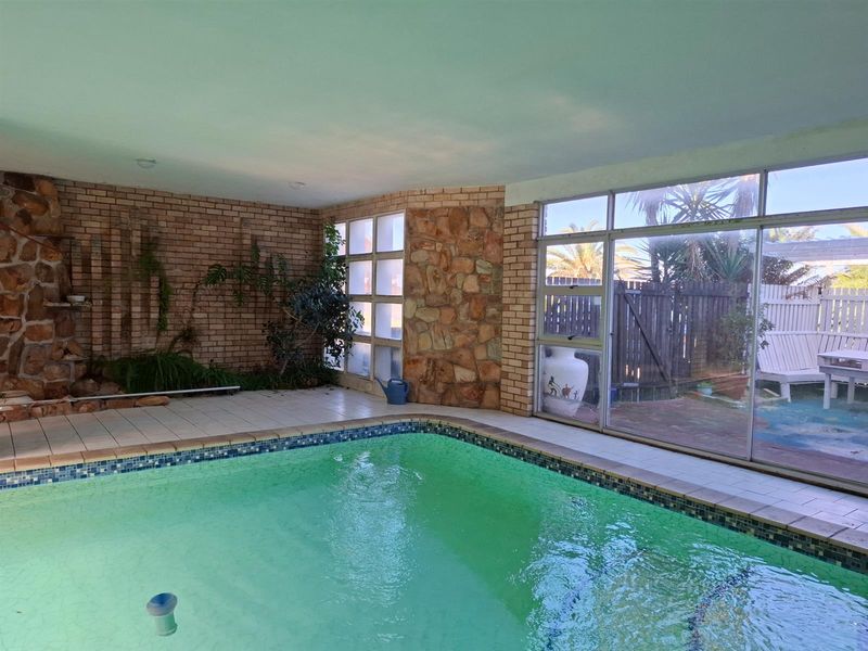 Indoor swimming pool area featuring a brick and stone feature wall, tiled surround, and large glass sliding doors leading to the rear garden.