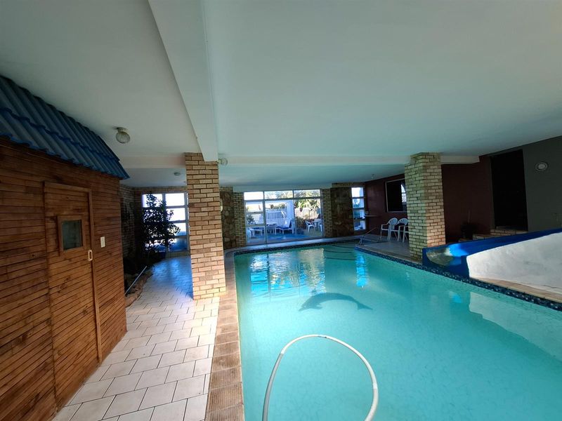 An indoor swimming pool area featuring brick columns, tiled flooring, a built-in slide, and an integrated sauna unit with direct access to the outdoor patio.