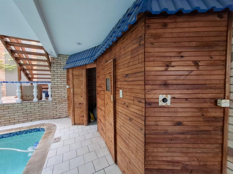 Outdoor pool area featuring a tiled surround, a timber-clad structure with a blue metal roof, and an adjacent staircase.