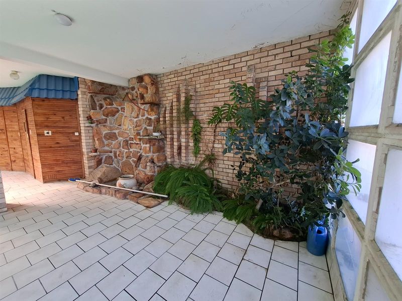A covered patio area featuring a brick and stone feature wall, tiled flooring, and a wooden door, offering a rustic outdoor space.
