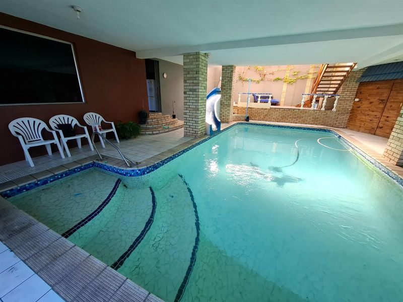 An indoor swimming pool area featuring brick columns, tiled steps, and a wooden staircase leading to an upper level.