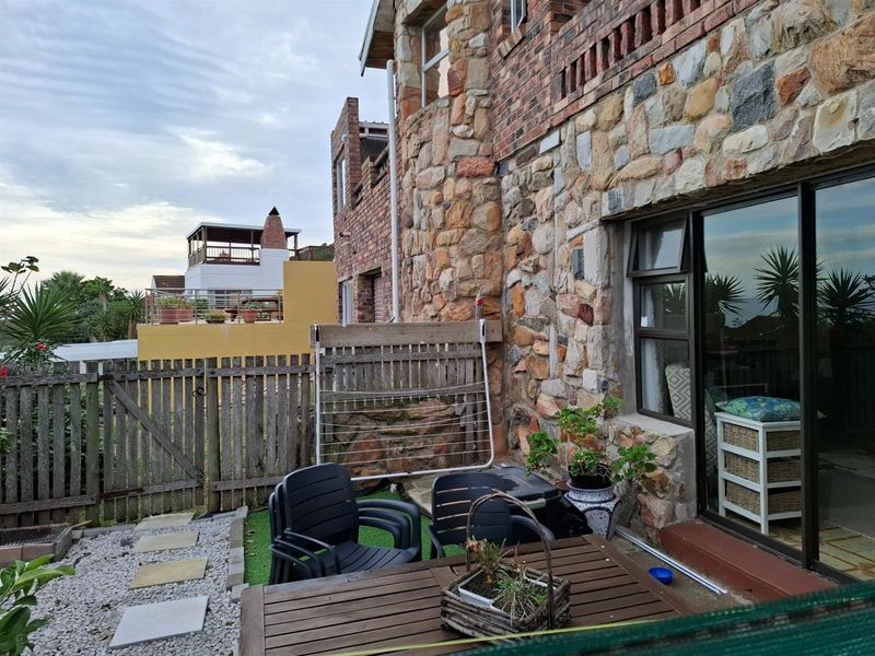 Rear exterior view of a multi-story home featuring rustic stone cladding, a sliding glass door, and a private garden area with a wooden fence.