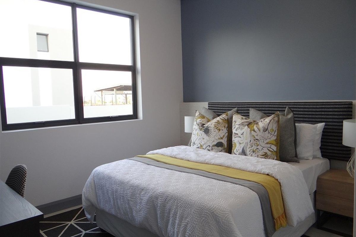 A well-maintained bedroom featuring a modern accent wall, large window for natural light, and integrated headboard design.