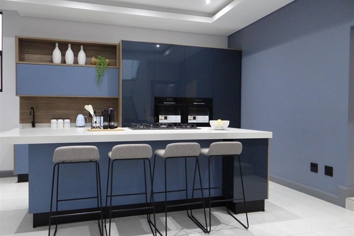 Modern kitchen featuring a central island with a built-in gas hob, sleek blue cabinetry, integrated double ovens, and recessed ceiling lighting.