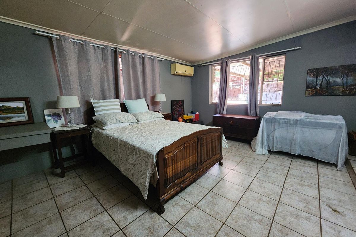 Spacious bedroom featuring tiled flooring, a wall-mounted air conditioning unit, and security bars on the windows.