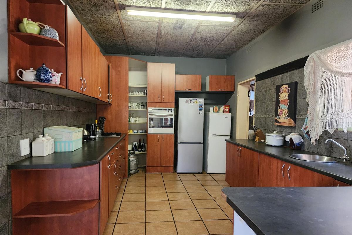 A functional kitchen featuring wood-look cabinetry, laminate countertops, built-in oven, and tiled flooring, offering potential for a modern renovation.