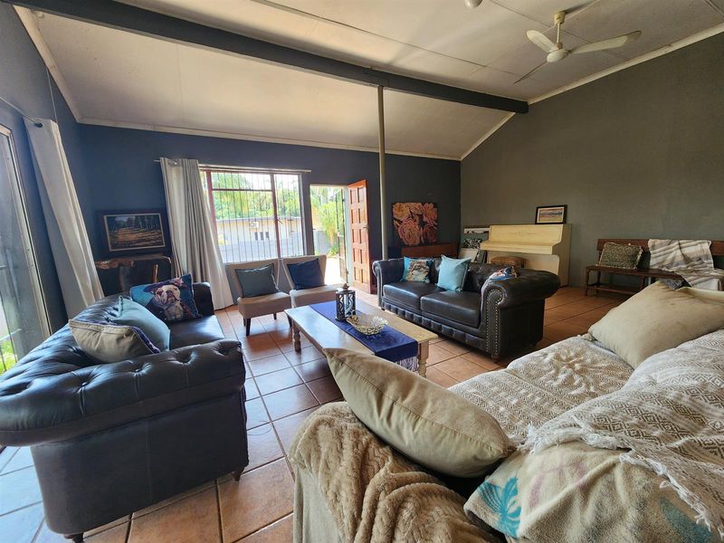 Spacious living room featuring tiled flooring, a ceiling fan, and an exposed structural beam, with direct access to the exterior through a security door.