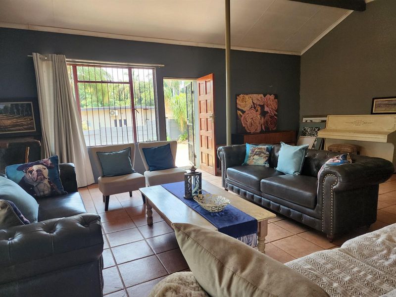 Spacious living room featuring tiled flooring, exposed ceiling beams, and direct access to the exterior through a timber door.