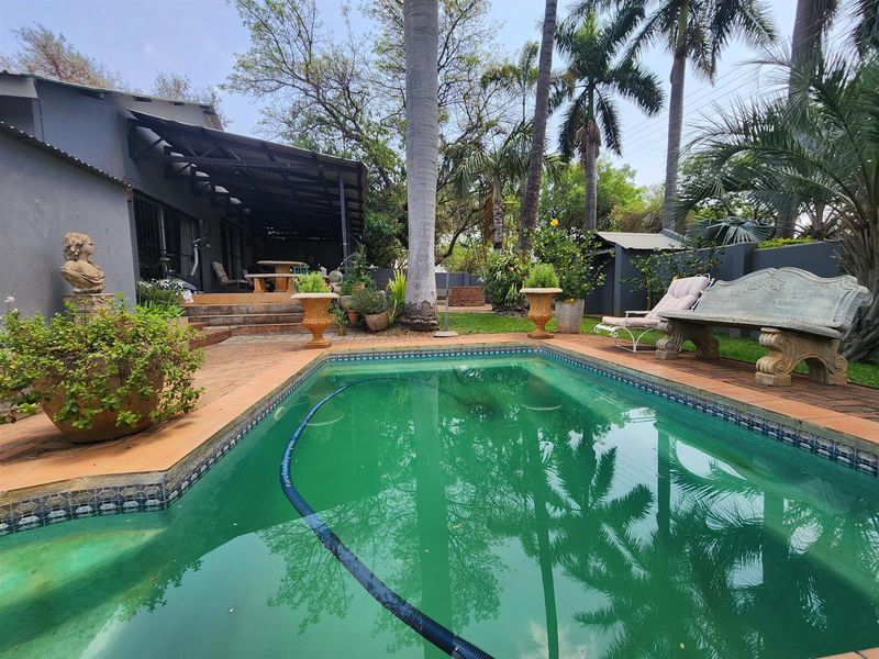Outdoor pool area featuring a swimming pool with tiled surround, adjacent covered patio, and established garden setting.