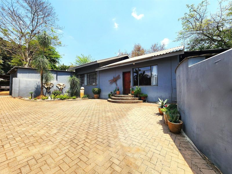Front elevation of a single-story house featuring a paved driveway, secure entrance with timber door, and established boundary walls.