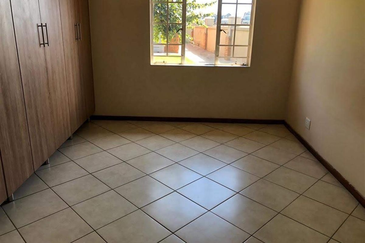 A bedroom featuring tiled flooring, built-in wooden cupboards, and a window providing natural light and a view of the exterior.