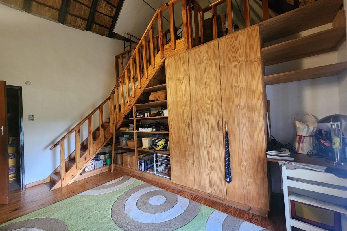 Bedroom featuring a timber staircase leading to a mezzanine level, with integrated timber cabinetry, shelving, and exposed thatched roof detailing.