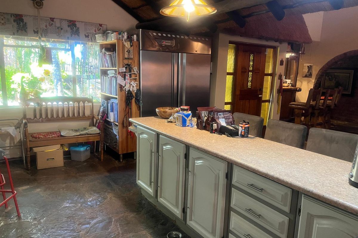 A rustic kitchen featuring a large island, stone flooring, and a traditional thatched ceiling with exposed timber beams.