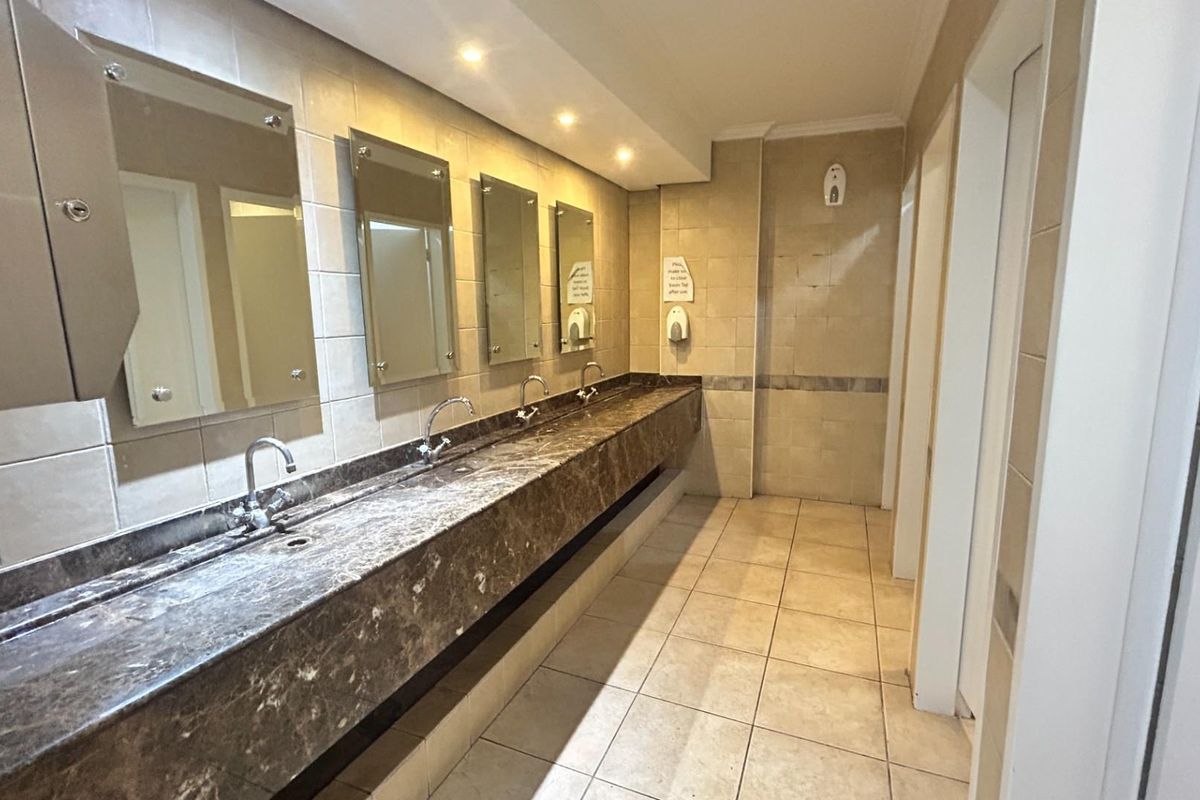 Commercial restroom featuring a long marble vanity with multiple integrated sinks, wall-mounted mirrors, and tiled flooring.