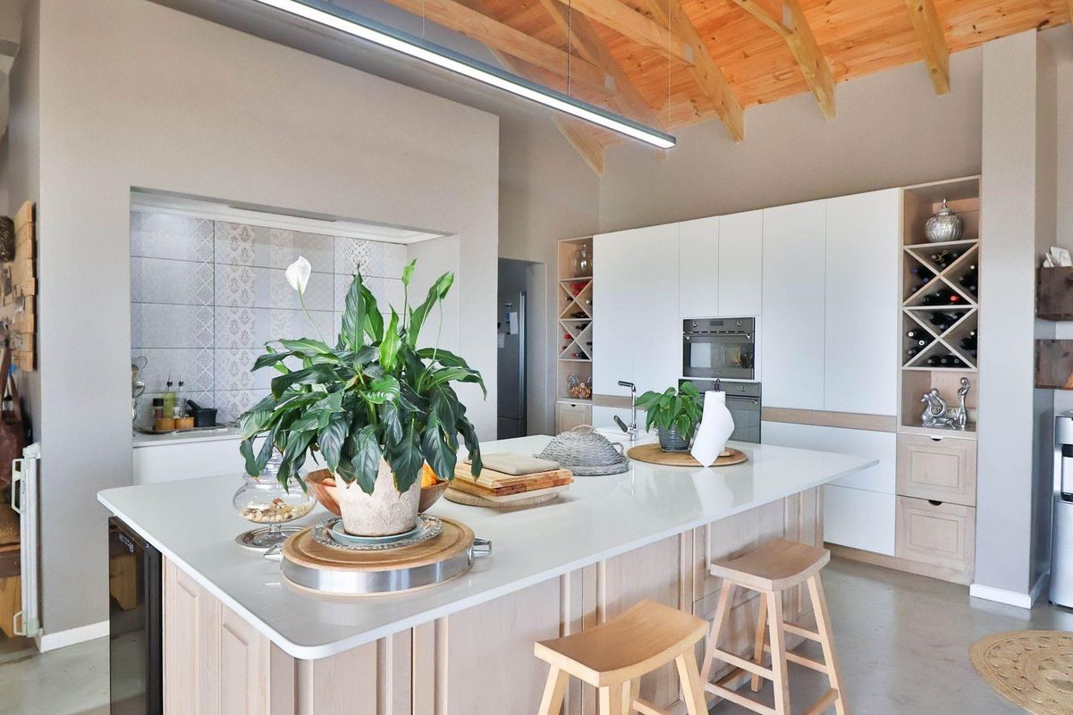 Modern open-plan kitchen featuring a large central island, sleek white cabinetry, built-in oven, and exposed timber vaulted ceiling beams.