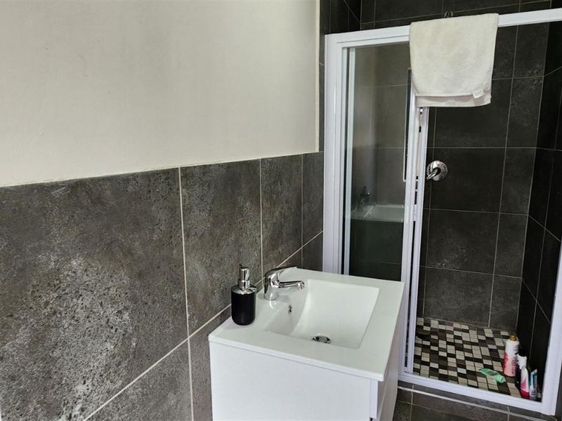 A modern bathroom featuring a vanity basin, a glass-enclosed shower with dark tiled walls, and contemporary floor tiling.