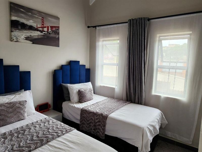 A well-maintained bedroom featuring two twin beds, neutral wall tones, and dual casement windows with fitted curtain rods.