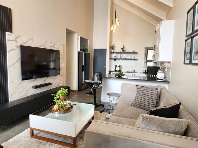 Modern open-plan living area featuring a vaulted ceiling, marble-look feature wall, and a functional kitchen with an island and floating shelves.