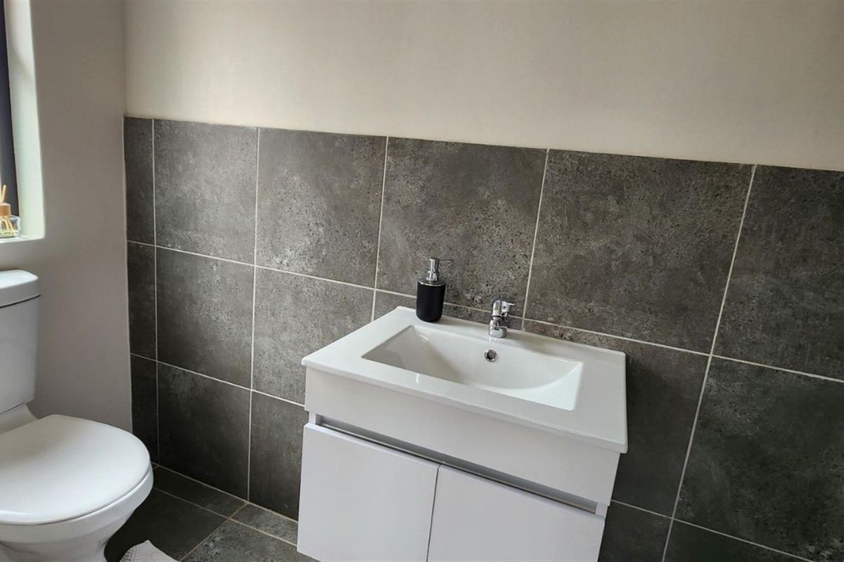 A clean, modern bathroom featuring a white vanity cabinet with a ceramic basin, chrome mixer tap, and a tiled splashback.