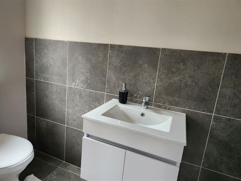 A clean, modern bathroom featuring a white vanity cabinet with a ceramic basin, chrome mixer tap, and a tiled splashback.