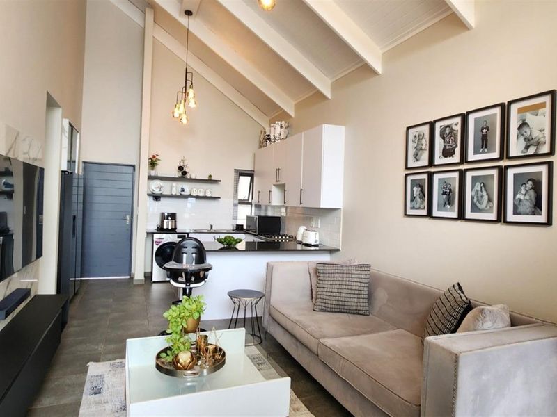 Modern open-plan living area featuring a vaulted ceiling with exposed rafters, sleek kitchen cabinetry, and contemporary tiled flooring.