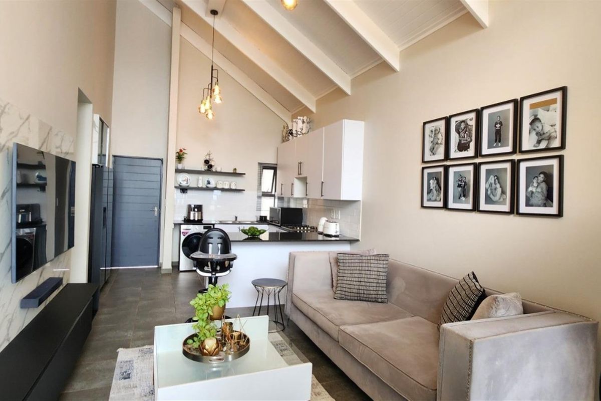 Modern open-plan living area featuring a vaulted ceiling with exposed rafters, sleek kitchen cabinetry, and contemporary tiled flooring.