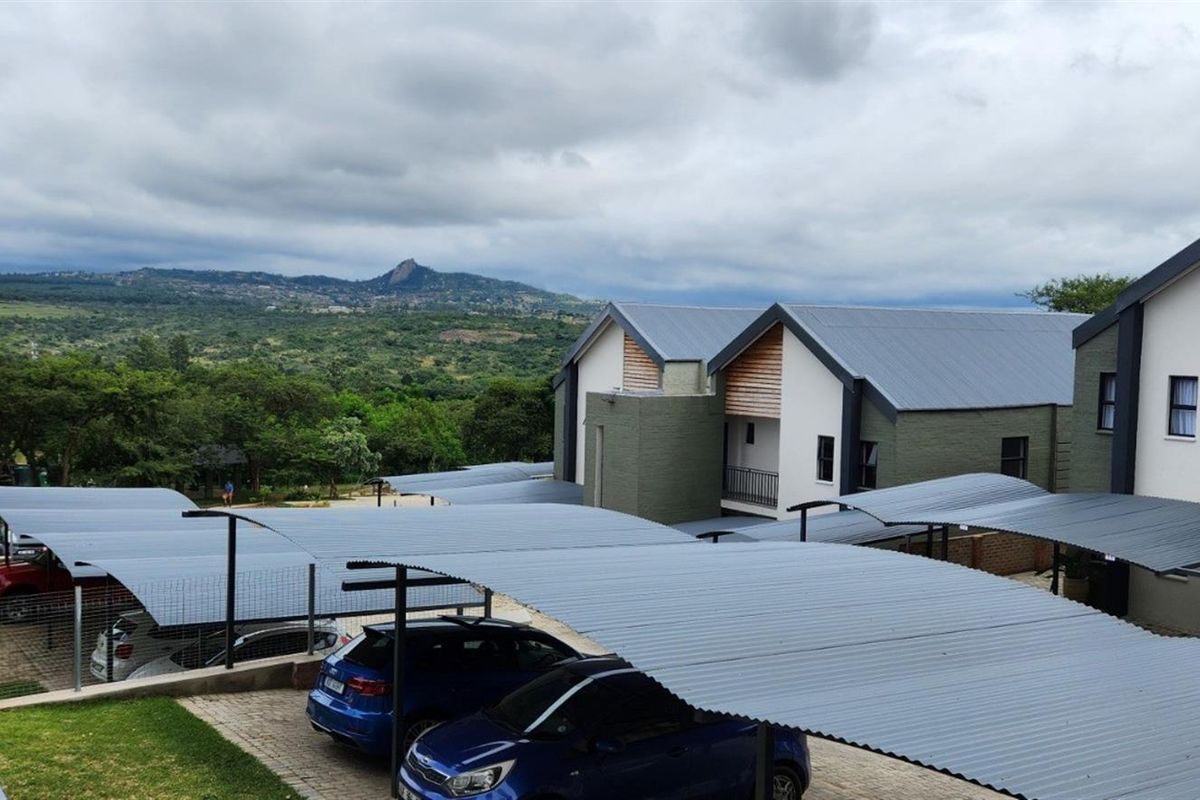 An elevated view of the townhouse complex featuring covered parking bays, paved driveways, and modern architectural finishes with scenic mountain views in the background.