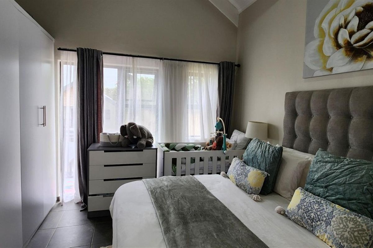 A well-lit bedroom featuring tiled flooring, a vaulted ceiling, and a large built-in wardrobe, offering a comfortable and functional living space.