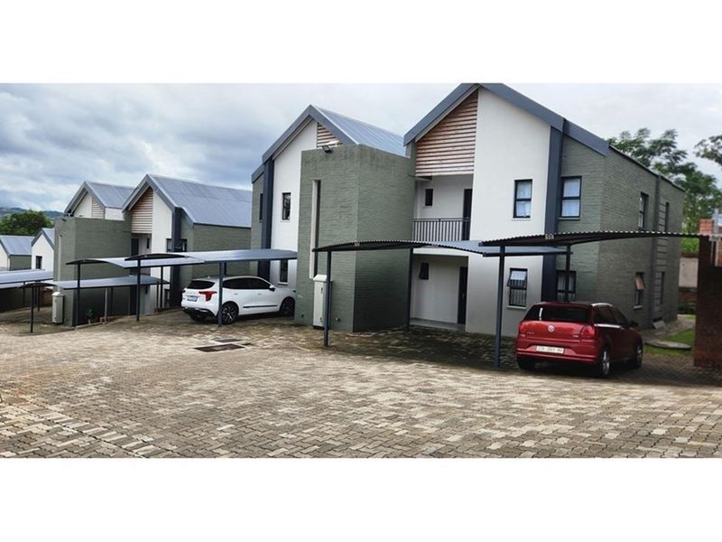 Front view of a townhouse complex featuring paved driveways, covered carports, and modern multi-story brick and metal roof architecture.