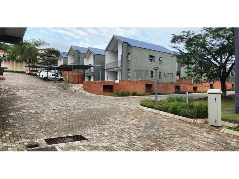A view of the townhouse complex entrance featuring paved driveways, covered parking bays, and modern brick and masonry building facades.