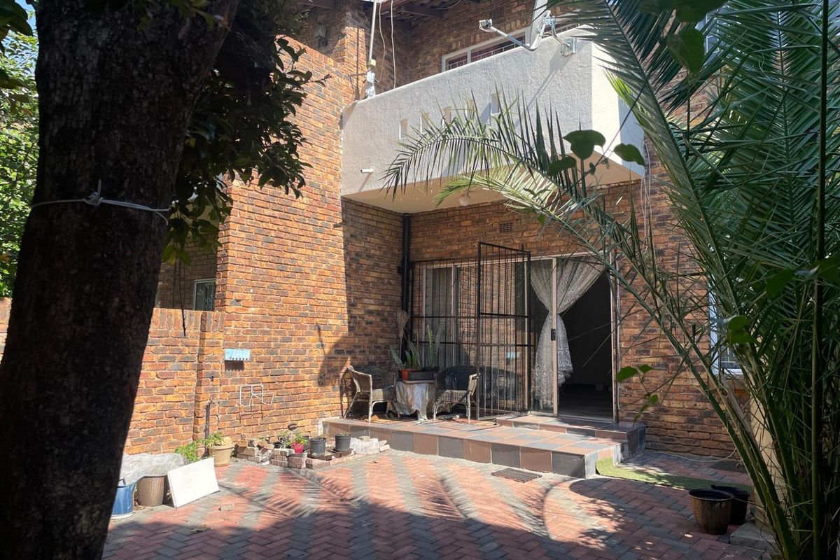 Rear view of the property featuring a brick facade, a paved patio area, and an upper-level balcony with access via a sliding door.